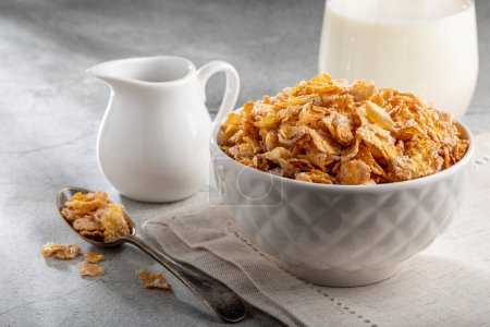 Corn flakes in bowl and glass of milk on table.