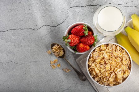 Corn flakes in the bowl with berries and milk on the table.