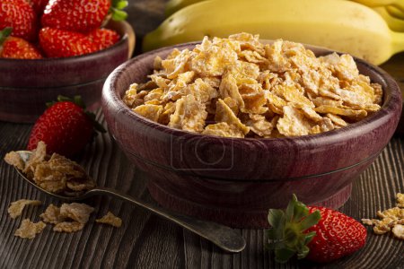 Corn flakes in the bowl with berries on the table.