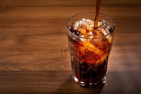 Cola-Glas mit Eiswürfeln auf Holztisch.