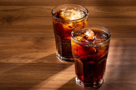 Coke glasses with ice cubes on wooden table.