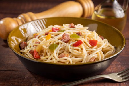 Plate with spaghetti, bacon and chopped vegetables.