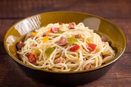 Assiette avec spaghettis, bacon et légumes hachés.