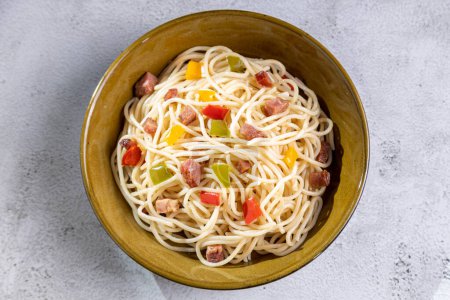 Plate with spaghetti, bacon and chopped vegetables.
