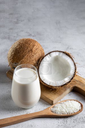 Téléchargez les photos : Verre de lait de coco avec des morceaux de noix de coco sur la table. - en image libre de droit