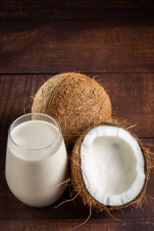 Glass of coconut milk with pieces of coconut on the table.