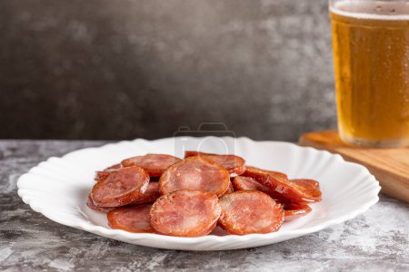 Sliced fried pepperoni sausage with glass of beer on the table