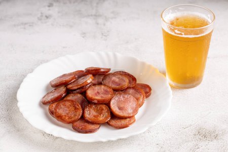 Embutido de pepperoni frito en rodajas con un vaso de cerveza sobre la mesa