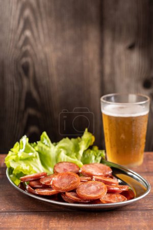 Foto de Embutido de pepperoni frito en rodajas con un vaso de cerveza sobre la mesa - Imagen libre de derechos