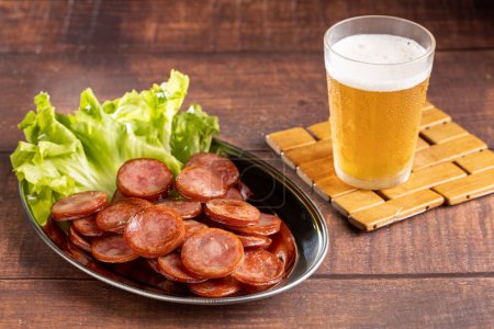 Sliced fried pepperoni sausage with glass of beer on the table