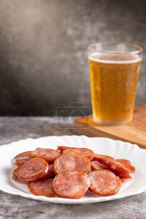 Embutido de pepperoni frito en rodajas con un vaso de cerveza sobre la mesa