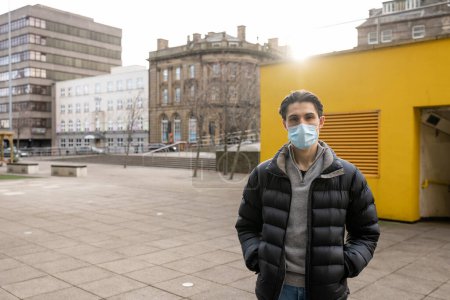 Photo for A young man spending the day in Newcastle Upon Tyne. He is standing on a paved area in the city centre. He is looking at the camera and wearing a protective face mask. - Royalty Free Image