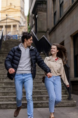 Photo for A young couple spending the day in Newcastle Upon Tyne together. They are holding hands and running through the city with steps behind them. - Royalty Free Image