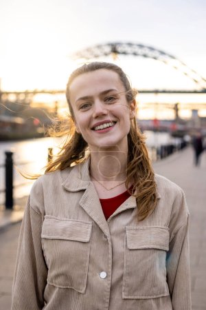Photo for A portrait of a young woman spending the day in Newcastle Upon Tyne. She is looking at the camera and smilling while the sun shines behind her. - Royalty Free Image