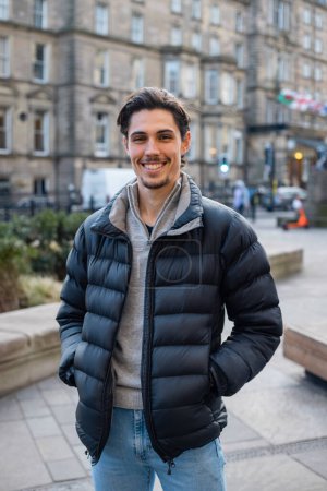 Photo for A young man spending the day in Newcastle Upon Tyne. He is standing on a paved area in the city centre with buildings behind him. He is looking at the camera and smiling. - Royalty Free Image