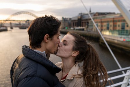 Photo for A close-up shot of a young couple standing side by side sharing a kiss together on a bridge in the city, they are in love. - Royalty Free Image