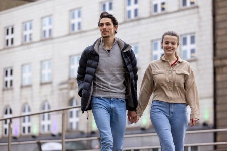 Photo for A wide-view shot of a young couple walking side by side together, they are holding hands and they're in love. - Royalty Free Image