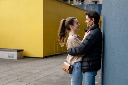 Photo for A side-view shot of a young couple standing face to face together against a wall, they are embracing and they're in love. - Royalty Free Image