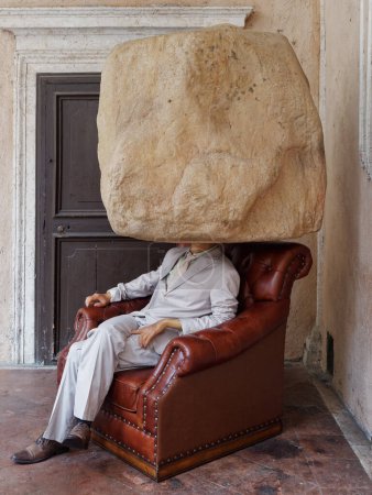 Foto de Roma, Italia - Marzo 2021: hombre de obra de arte sentado en un sillón con una gran piedra en lugar de la cabeza - Imagen libre de derechos