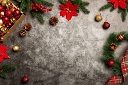 Foto de Corona de Navidad en la mesa de piedra. Caja con adornos de adornos de bolas rojas y doradas de Navidad. Tarjeta de felicitación de fondo con ramas de abeto y Poinsettias - Imagen libre de derechos