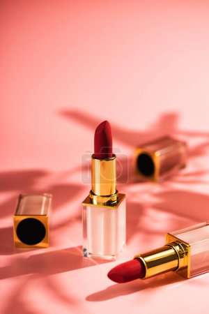 Red lipstick beauty product on a pink background. Sun shadows from flowers, copy space Poster 647093440