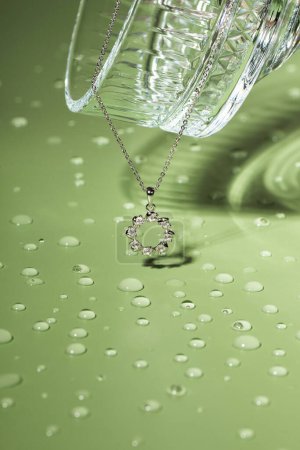 Stylish silver necklace and Champagne glass on green background with water drops. Copy space for text
