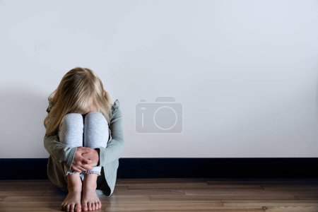 Foto de Child abuse, violence concept - young girl scared sitting on the floor. High quality photo - Imagen libre de derechos