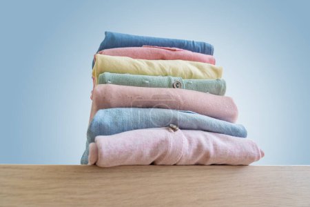 Téléchargez les photos : Empilement de vêtements propres pour femmes fraîchement lavés et soigneusement pliés sur une table en bois. Pile de chemises et de pulls sur la table - en image libre de droit