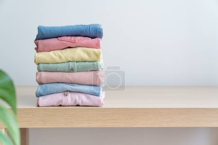 Foto de Montón de ropa limpia para mujer recién lavada y cuidadosamente doblada sobre una mesa de madera. Montón de camisas y suéteres sobre la mesa - Imagen libre de derechos