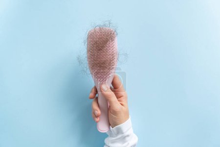 Photo for Hair loss concept - female hand holding brush with lost hair, blue background - Royalty Free Image