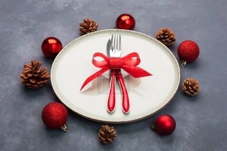 Foto de Ajuste de mesa de Navidad que consta de un plato y cubiertos atados con un lazo y decoraciones de Navidad, sobre fondo azul - Imagen libre de derechos
