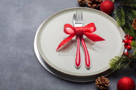 Photo for Christmas table setting consisting of a plate and cutlery tied with a bow. Side view with copy space, on blue background - Royalty Free Image