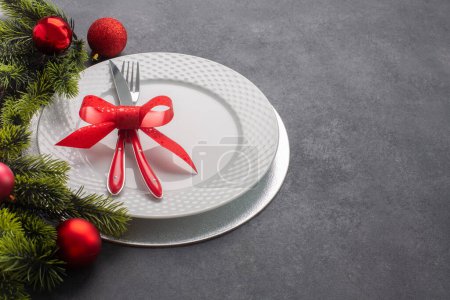 Téléchargez les photos : Ensemble de table de Noël composé d'une assiette blanche et de couverts attachés avec un arc. Vue latérale, sur fond sombre avec espace de copie - en image libre de droit