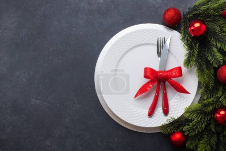 Photo for Christmas table setting consisting of a white plate and cutlery tied with a bow. Top view, on dark background with copy space - Royalty Free Image
