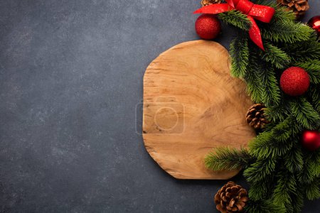 Foto de Ajuste de mesa de Navidad que consta de una tabla de cortar de madera y cubiertos atados con un lazo. Vista superior, sobre fondo oscuro con espacio para copiar - Imagen libre de derechos