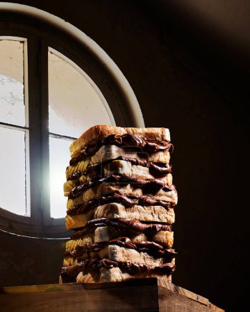 Foto de Large chocolate cream sandwich consisting of several pieces of toasted bread against a window. High quality creative photo - Imagen libre de derechos