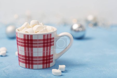 Foto de A cup of hot chocolate with marshmallows on a blue background with silver Christmas decorations on the table. High quality photo - Imagen libre de derechos