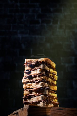 Téléchargez les photos : Large chocolate cream sandwich consisting of several pieces of toasted bread against a brick wall. High quality creative photo - en image libre de droit
