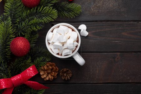 Photo for Red mug with hot chocolate on top of which pieces of marshmallows, and behind are branches of a Christmas tree decorated with red balls. Top view copy space - Royalty Free Image