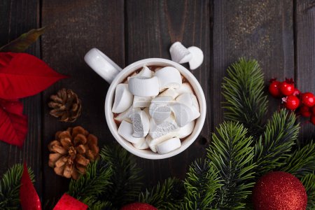 Foto de Red mug with hot chocolate on top of which pieces of marshmallows float, and behind are branches of a Christmas tree decorated with red balls. Top view - Imagen libre de derechos