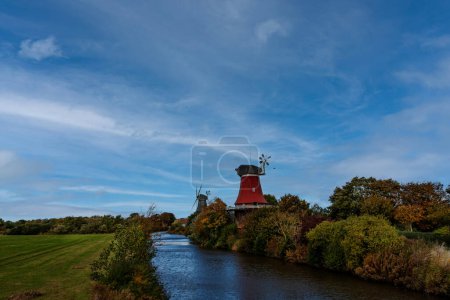 Téléchargez les photos : Les deux moulins à vent en rouge et noir se dressent au bord de la rivière. Le ciel bleu gît sur la scène idyllique - en image libre de droit
