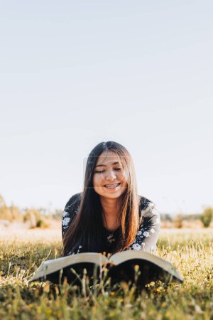 Foto de Young religious christian girl holding and reading her bible, outside in the field at sunset. High quality photo - Imagen libre de derechos