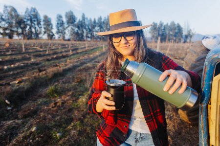 Photo for Young latin woman drinking mate in a natural space, on top of a little tractor. Latin beverage. Ethnical concept. High quality photo. Horizontal - Royalty Free Image