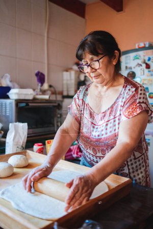 Photo for Portrait of an elderly latin woman cooking homemade bread in her kitchen. High quality photo - Royalty Free Image