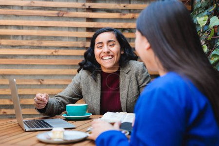 Téléchargez les photos : Conversation sur la sécurité financière : Une jeune Latina vend de l'assurance-vie à une autre femme dans un café confortable. Photo de haute qualité - en image libre de droit