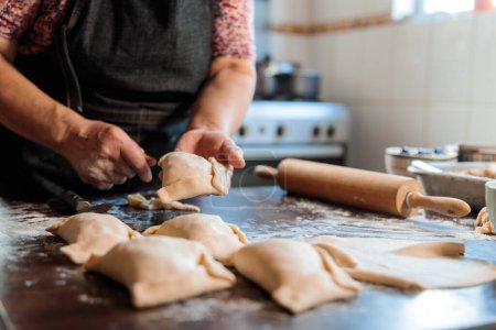 Saveurs du patrimoine : Femme âgée latine Préparer des empanadas chiliennes de boeuf cuit au four dans la chaleur de sa cuisine maison. Photo de haute qualité