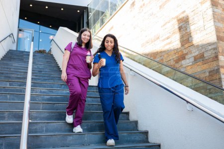 Two young health workers women leaving clinical building or hospital. They are nurses or medical professionals wearing scrubs. After work concept High quality photo