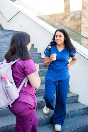 Two young health workers women leaving clinical building or hospital. They are nurses or medical professionals wearing scrubs. After work concept High quality photo