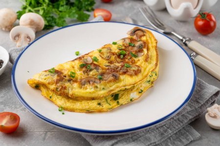Photo for Omelet with fried mushrooms and fresh herbs in a plate on a concrete background. Delicious healthy breakfast. Top view. Copy space - Royalty Free Image