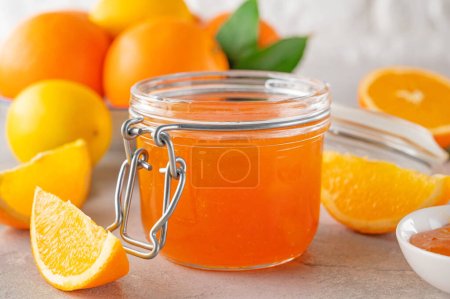 Orange marmalade or orange jam in a pot with fresh fruits on a gray background. Copy space.